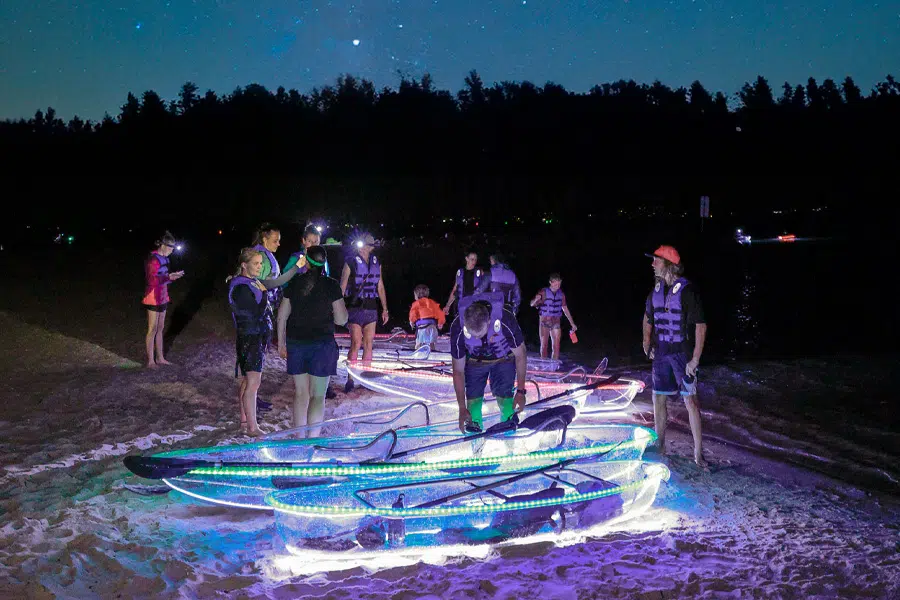 Kayakers standing around clear kayaks with lights at night